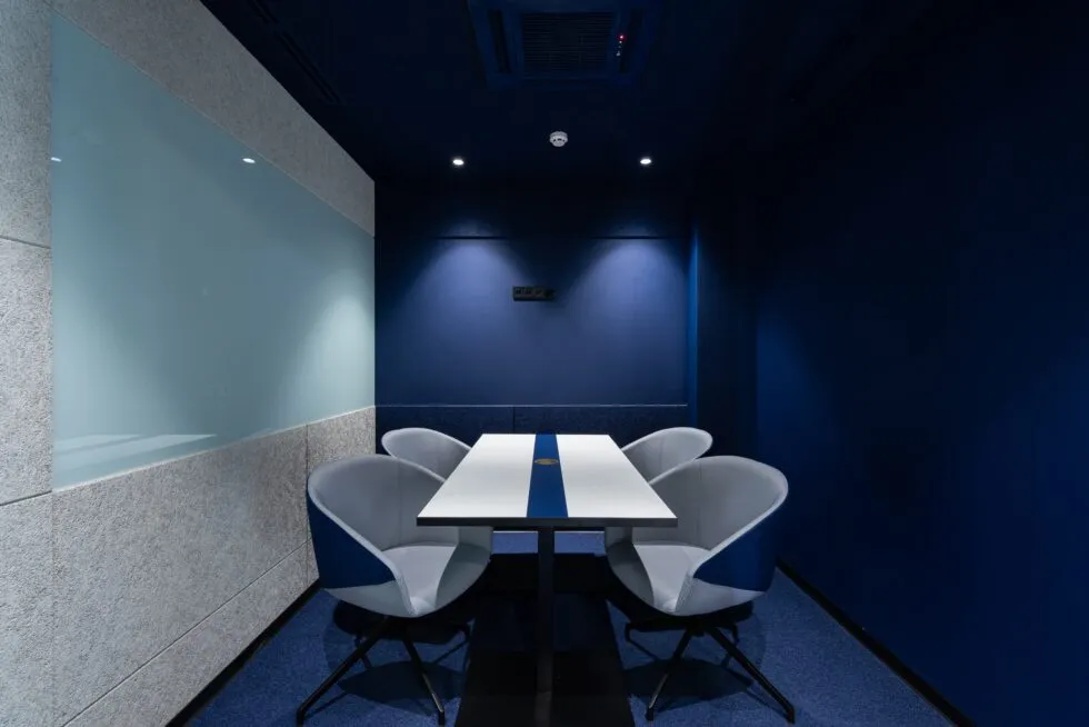 A modern conference room with blue walls, a white table, and four ergonomic chairs.