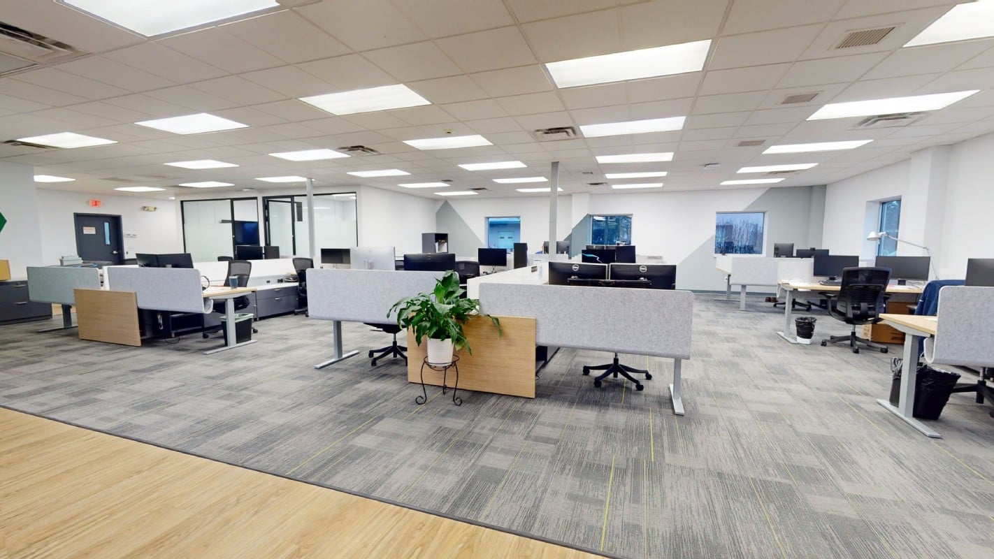 An empty office space with rows of desks, chairs, and natural light coming through windows.