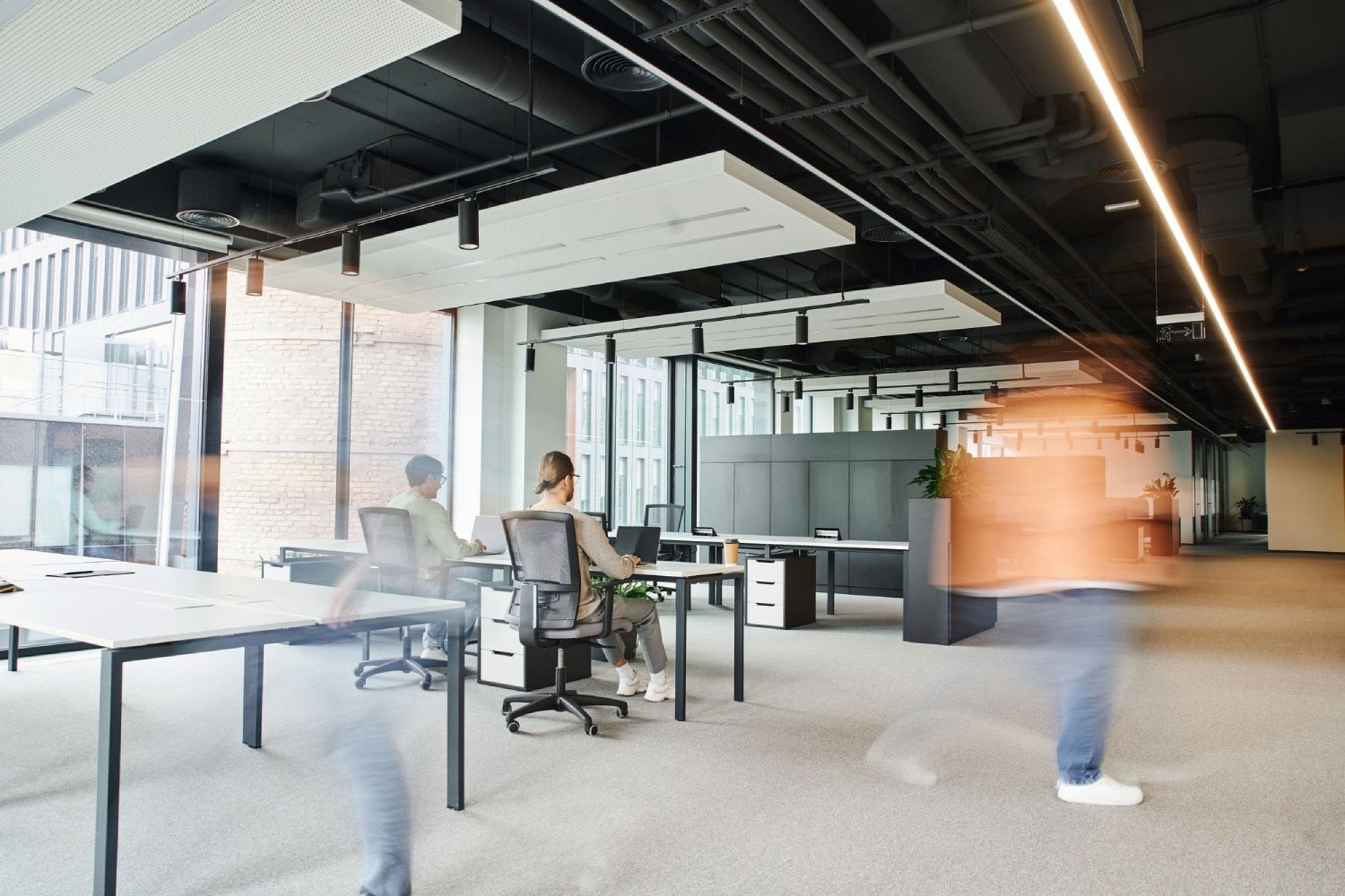 A modern office space with workers at desks and blurred motion of people walking.