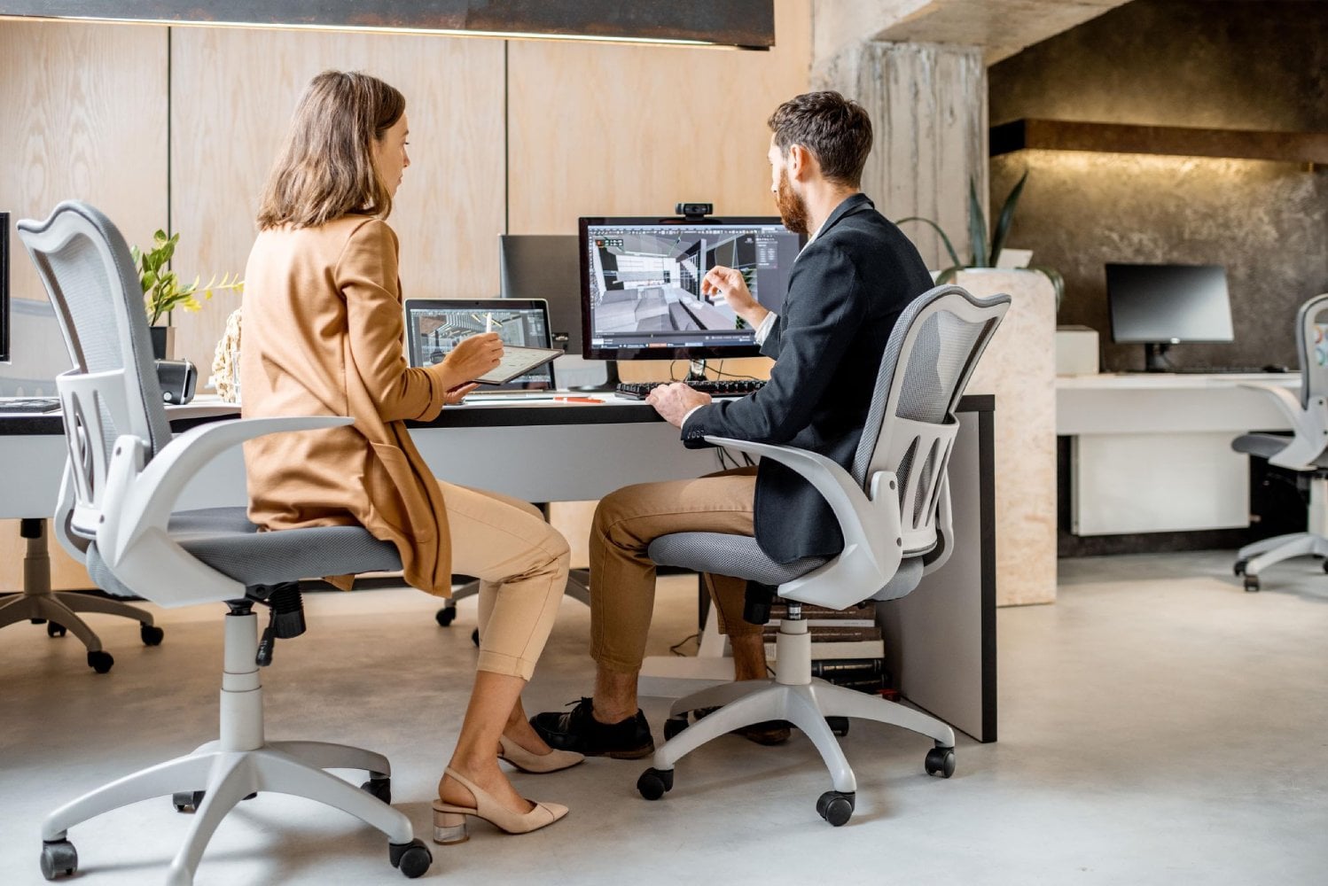 Two people working at a modern office desk, discussing designs on a computer screen.