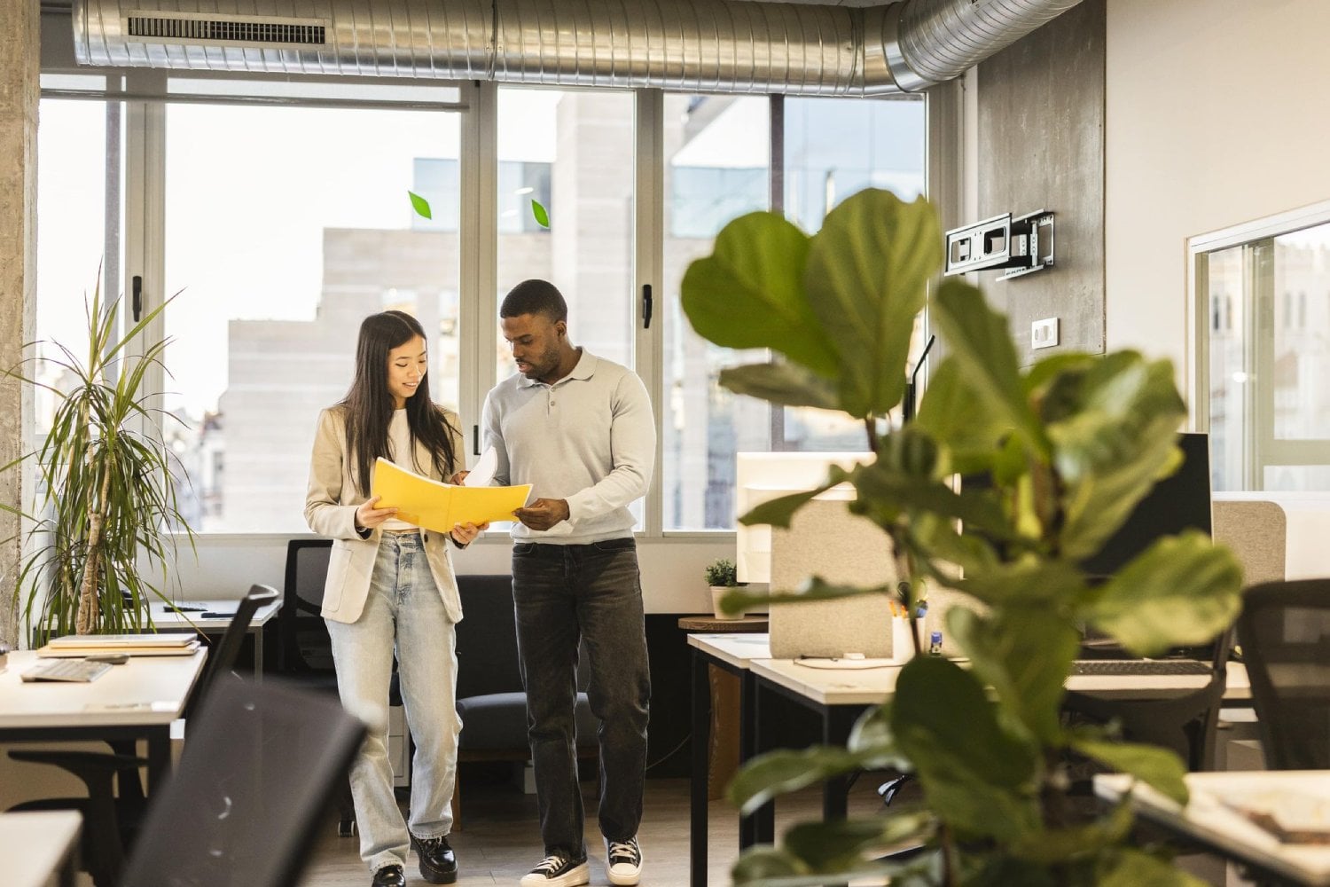 Two professionals, a woman and a man, are collaborating in a modern office space, reviewing documents together.