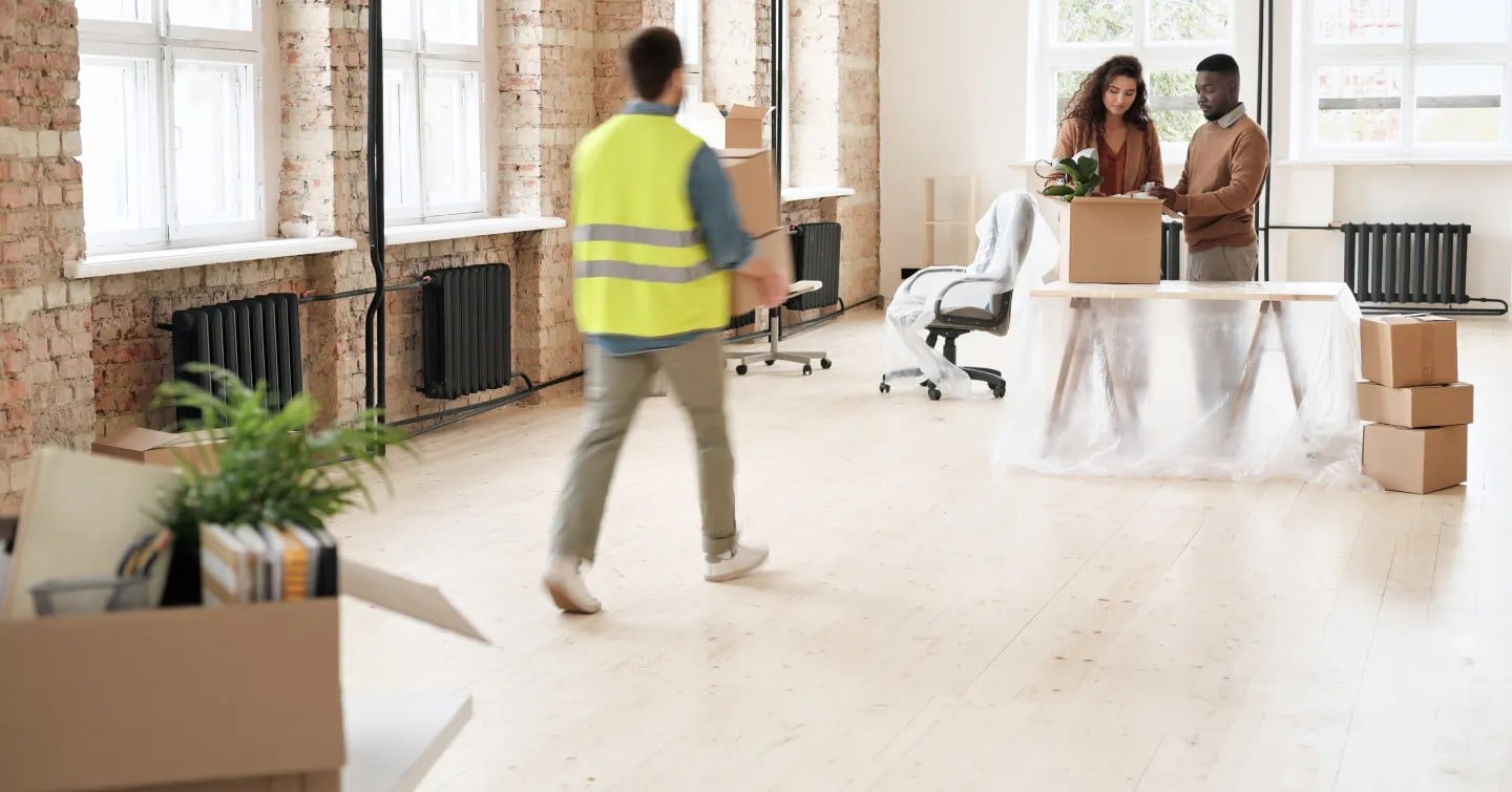 A man and woman are collaborating to move cardboard boxes in a modern office setting.