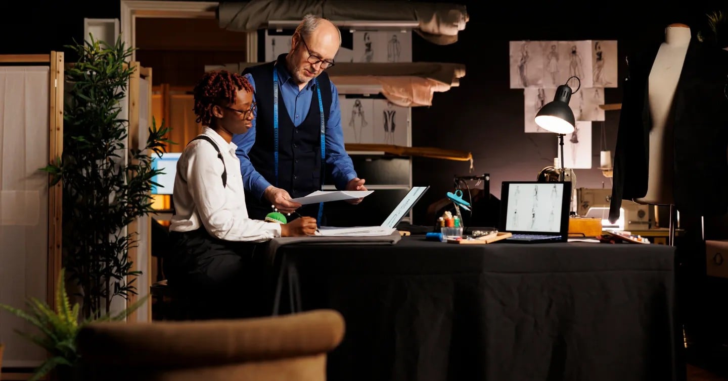Two individuals collaborate on a laptop in a well-lit room, focused on their work.