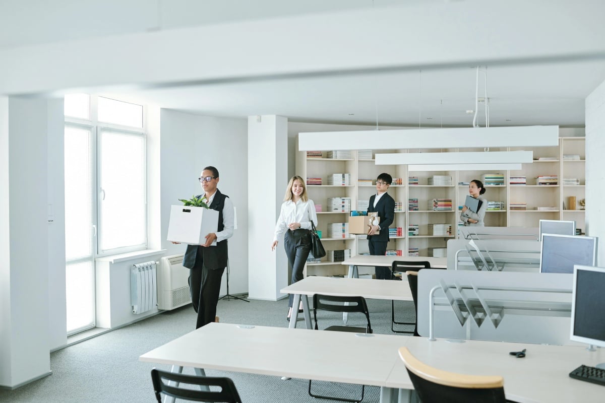 A diverse group of professionals collaborating in an office with desks and computers, engaged in discussion and work.