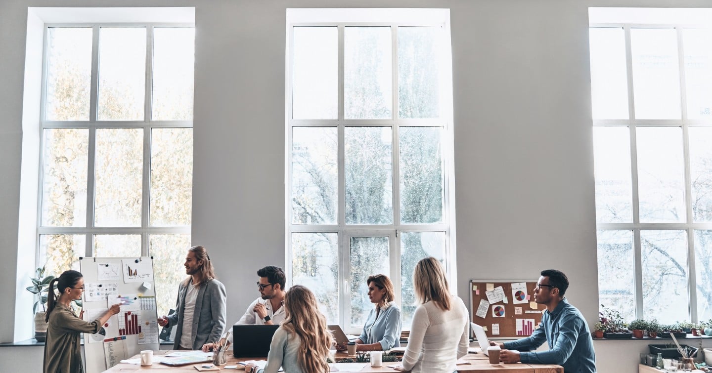 Several colleagues in an office, working together on a project, with laptops and documents spread across the table.