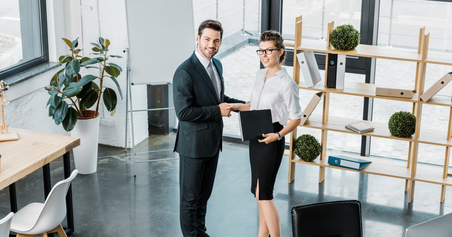Two business professionals shaking hands in a modern office setting, symbolizing a successful partnership or agreement.
