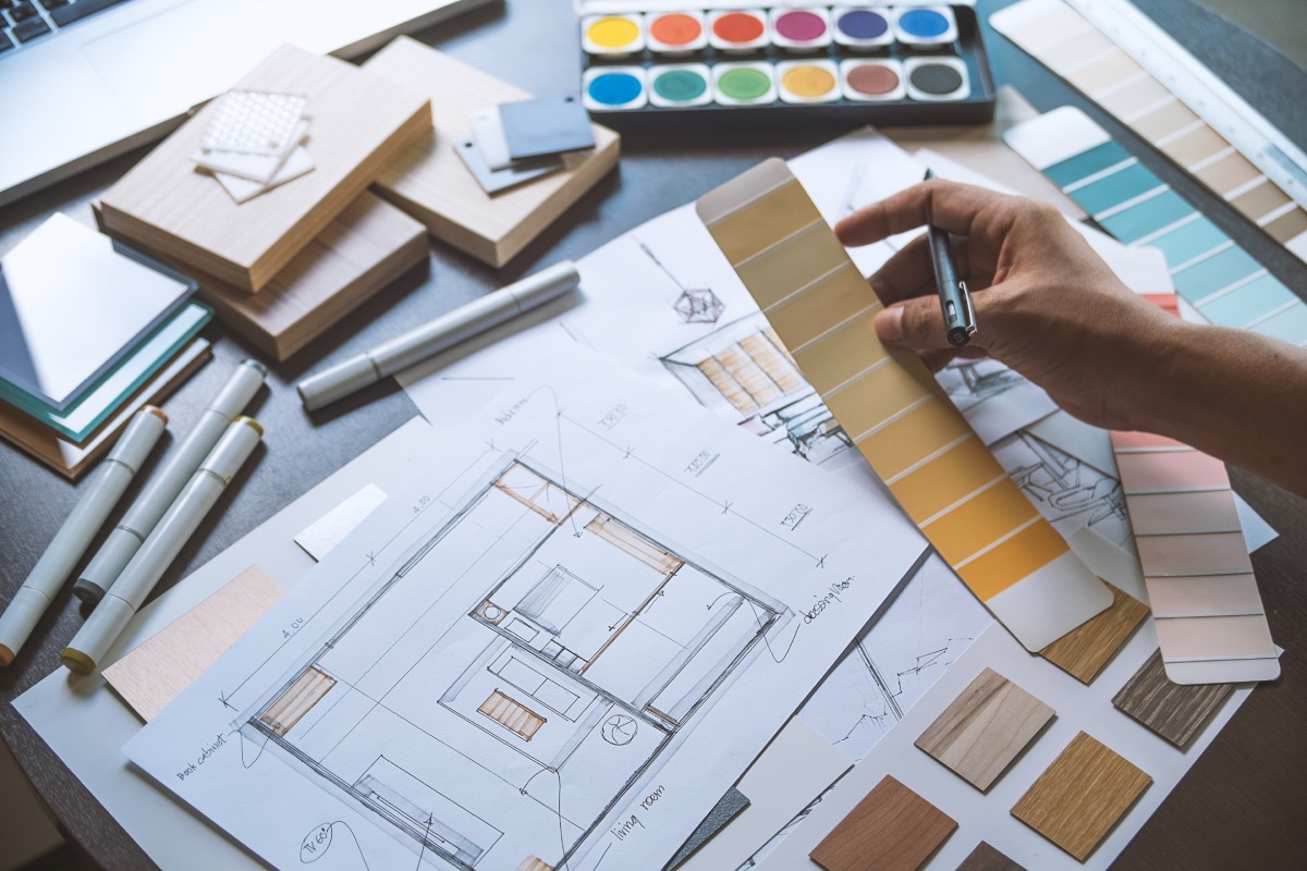 A designer sketches on a pad while using a laptop, showcasing a creative workspace with tools for design.