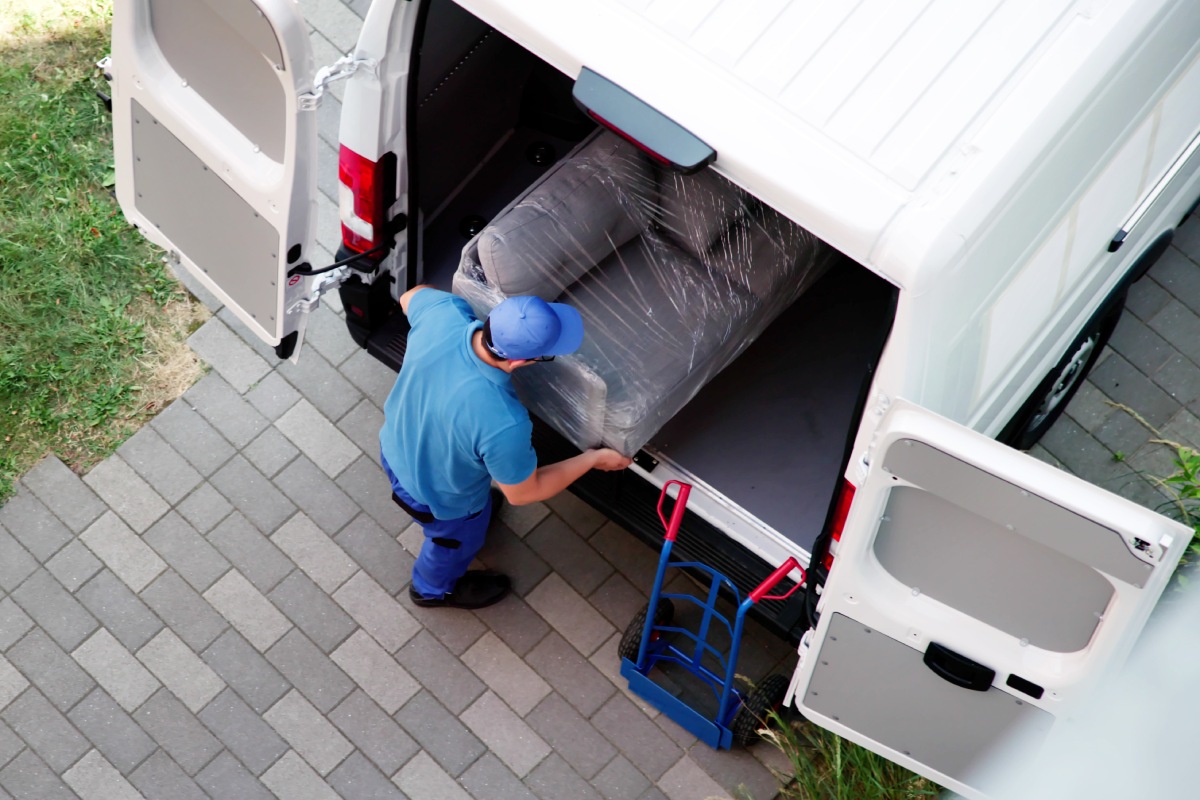 A man loads a large couch into a van, preparing for transportation.