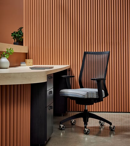 A desk and chair positioned in front of an orange wall, creating a vibrant workspace atmosphere.