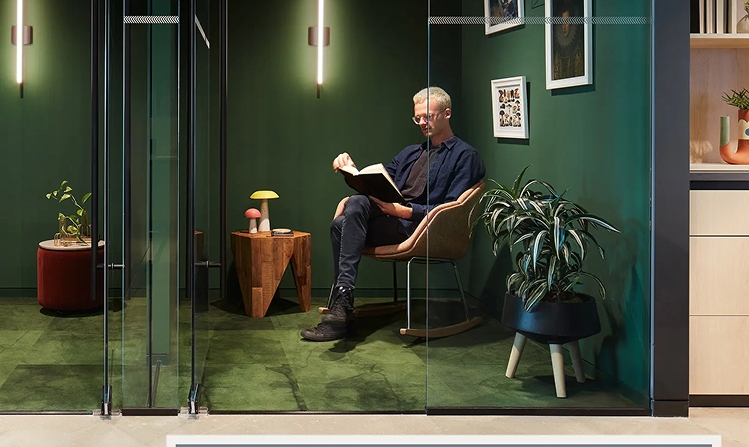 A man sits comfortably in a chair against a backdrop of a green wall in a cozy room.