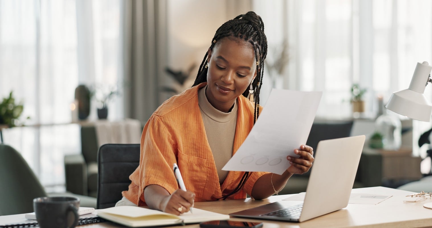 Black woman in home office, documents and laptop for research in remote work, ideas and thinking. Happy girl at desk with computer, writing notes and online search in house for freelance networking