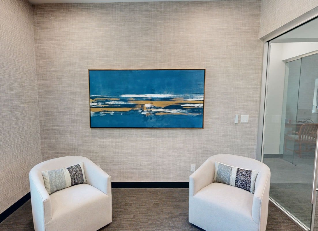 A modern interior space featuring two white armchairs facing a blue abstract painting on the wall.