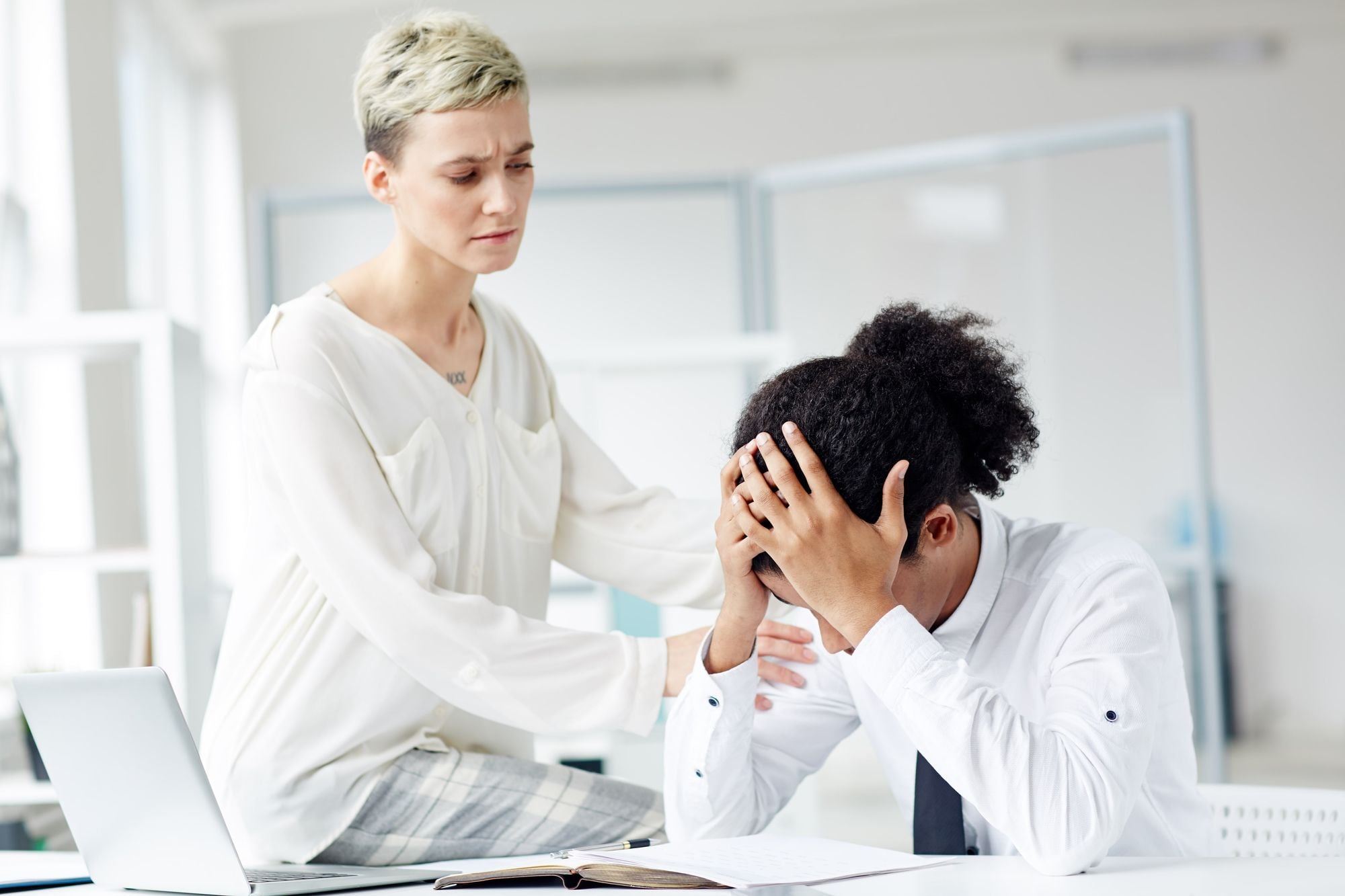 A woman comforting a distressed person at a desk in an office setting.