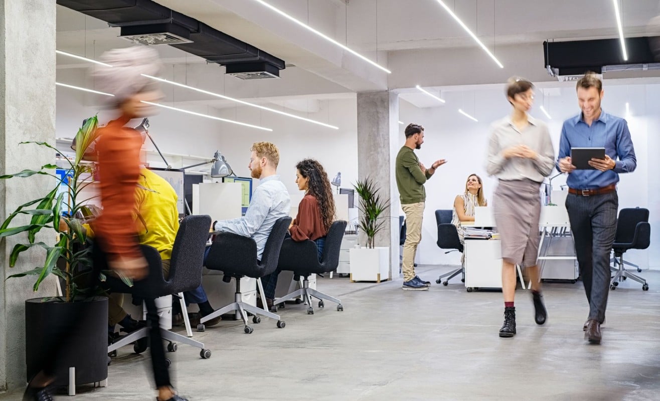 A modern office environment with several people working at desks, some collaborating, and others walking around.