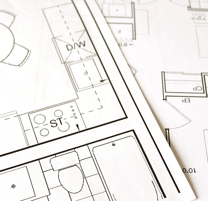 Close-up of printed architectural blueprints displaying a home floor plan with labeled fixtures like "D/W", "ST", a toilet, and a bathtub.