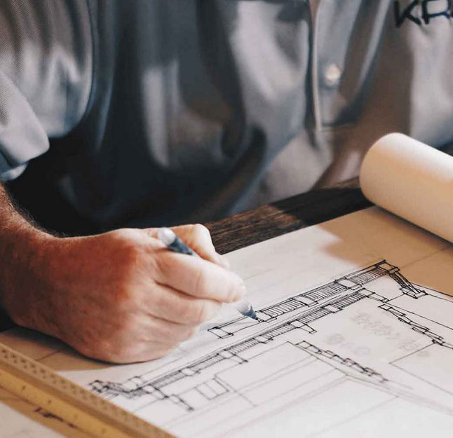 Close-up of an architect or designer's hand using a pen to sketch a detailed technical blueprint on paper.