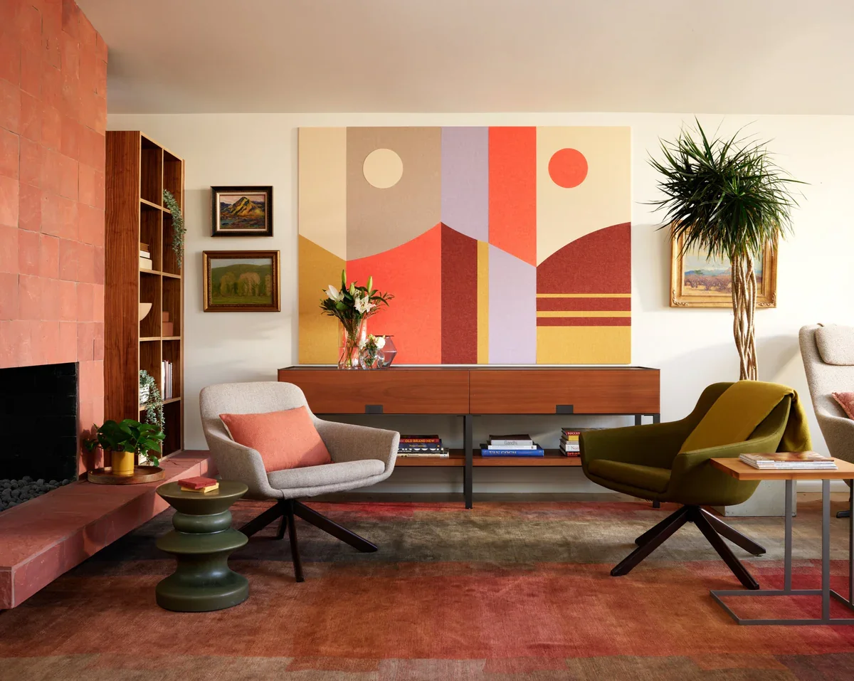A mid-century modern living room featuring a terracotta tile fireplace hearth, a large geometric abstract art piece above a wood credenza, two swivel armchairs, and a warm-toned patterned area rug.
