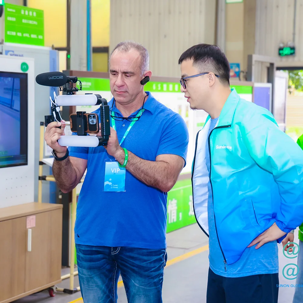 Two men examining a smartphone setup attached to a professional camera rig and light ring in an industrial office or warehouse setting.